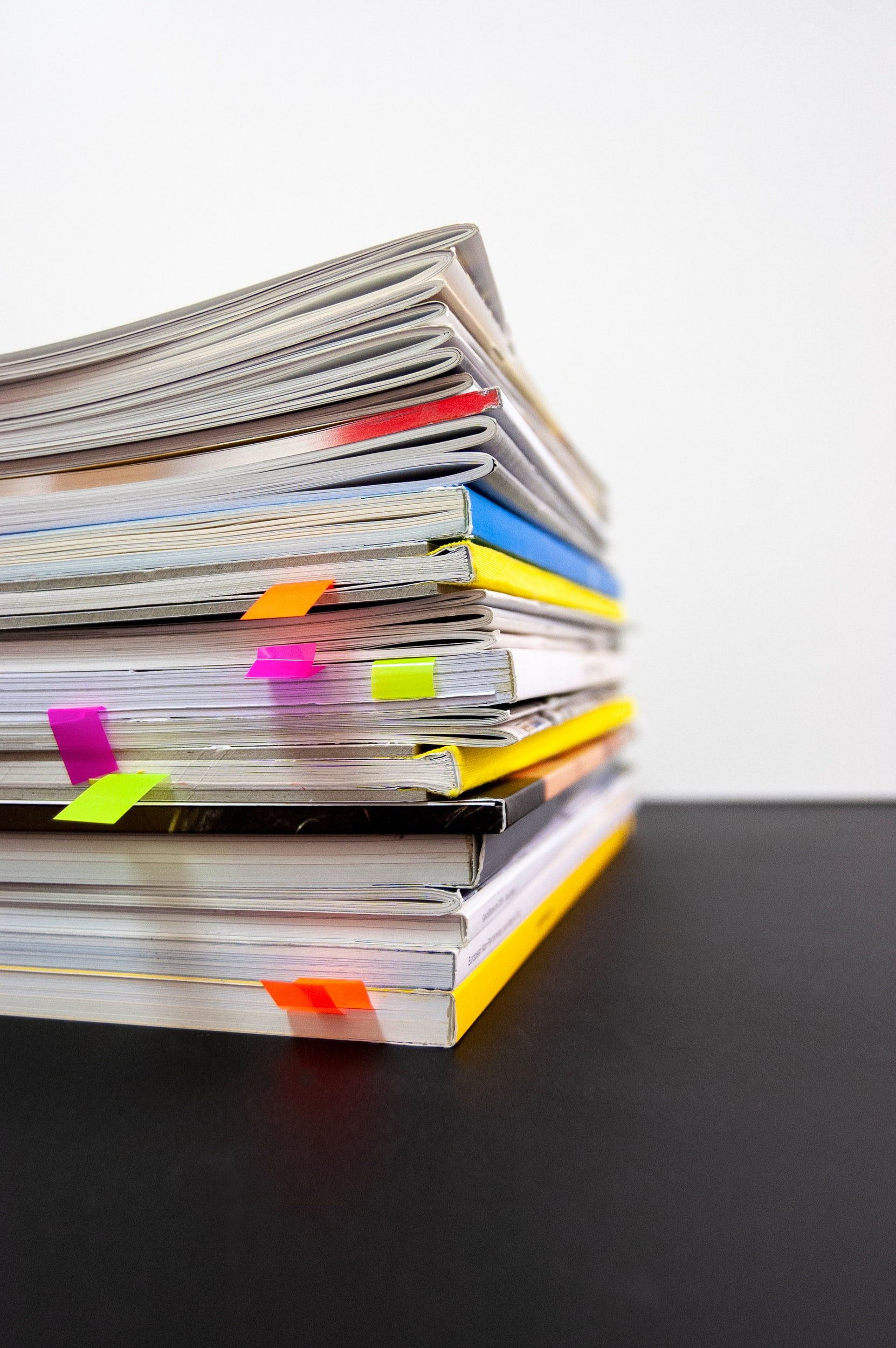 Stack of various notebooks and documents with colorful sticky notes on a black surface.